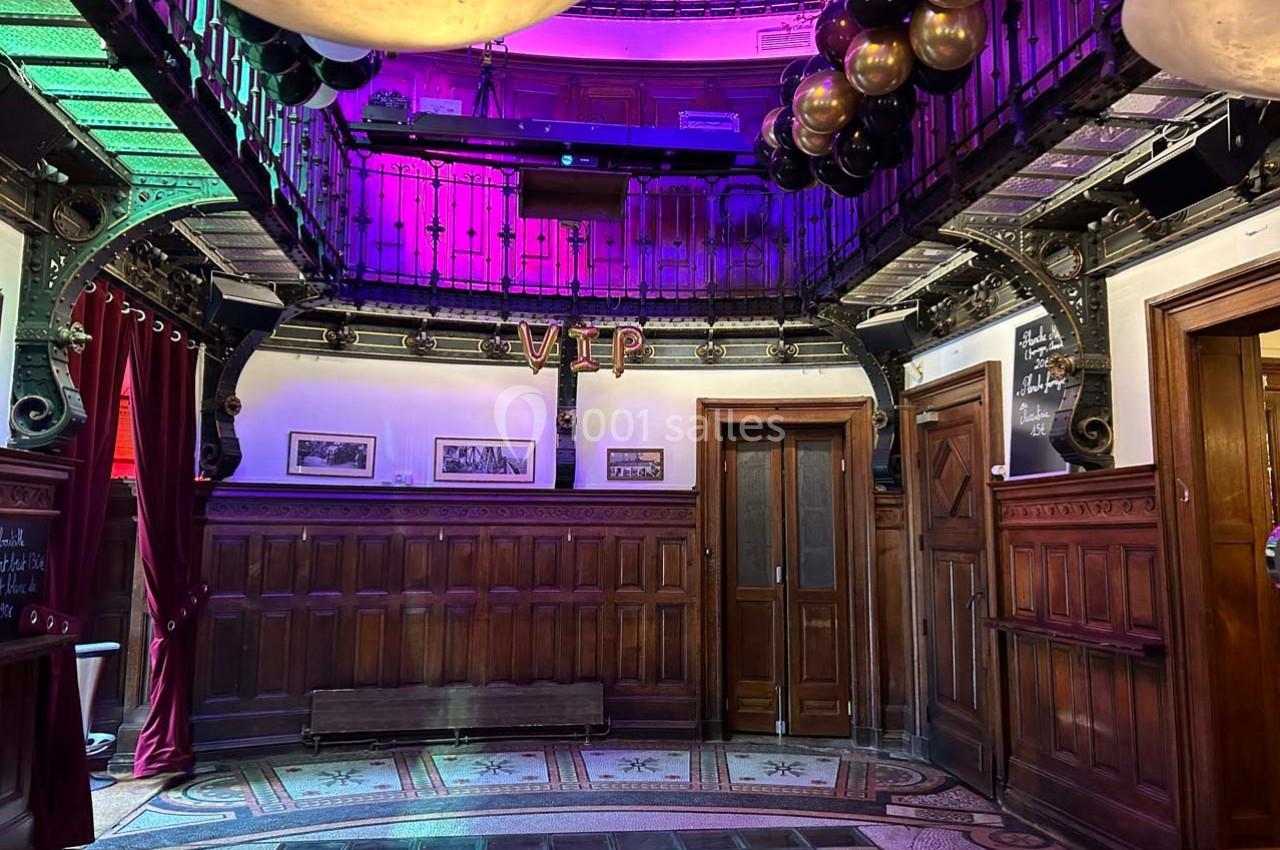 Salle décorée avec des ballons noirs et dorés, éclairage coloré, boiseries et balcon métallique en hauteur.