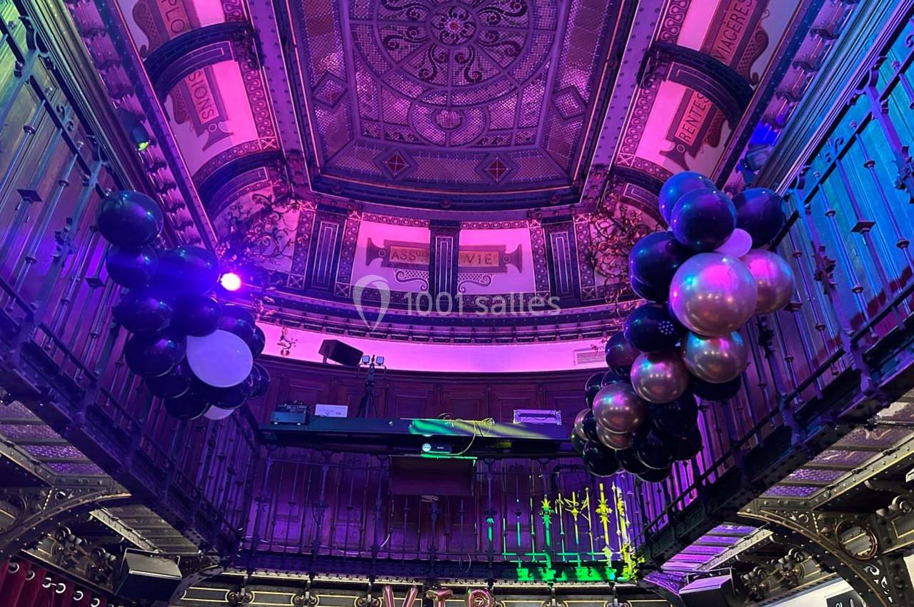 Plafond décoratif d'une salle avec balustrades, ballons noirs et métalliques suspendus, éclairage coloré.