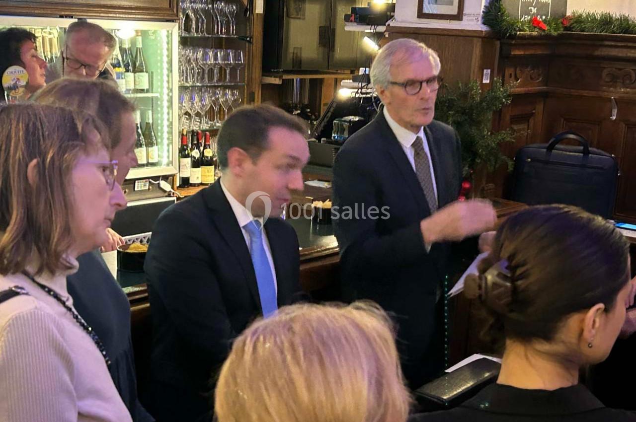 Un groupe de personnes échange autour d'un comptoir dans un bar ou un restaurant, avec des bouteilles en arrière-plan.