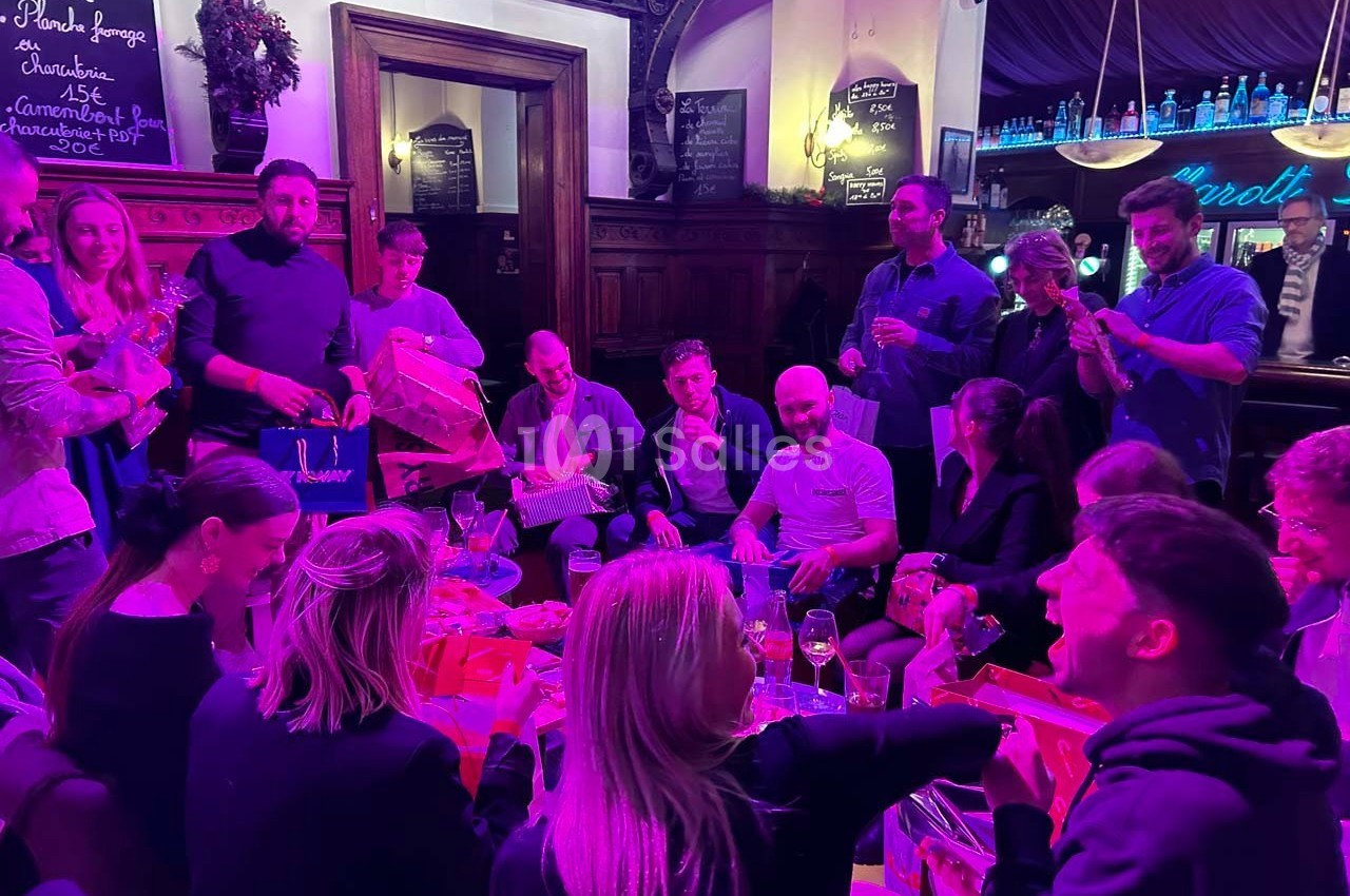 Un groupe de personnes assises et debout dans un bar, échangeant des cadeaux dans une ambiance chaleureuse et festive.