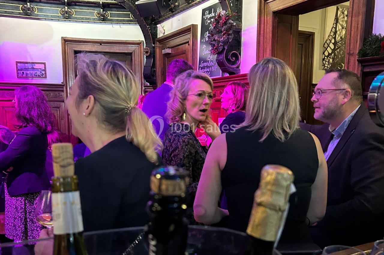Des personnes discutent dans un bar ou un espace événementiel, avec des bouteilles au premier plan et un éclairage coloré.