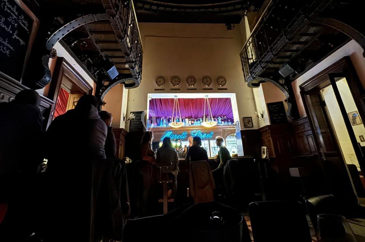 Intérieur d'un bar avec des clients assis au comptoir éclairé, entouré de décorations en bois et métal.