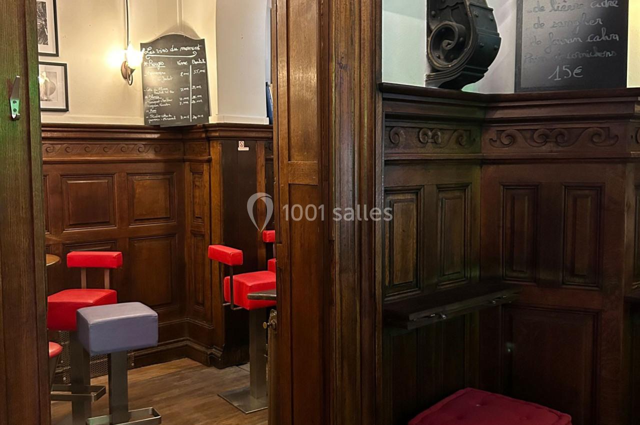 Intérieur d'un café avec des tabourets rouges, boiseries sombres et ardoises affichant des menus écrits à la craie.