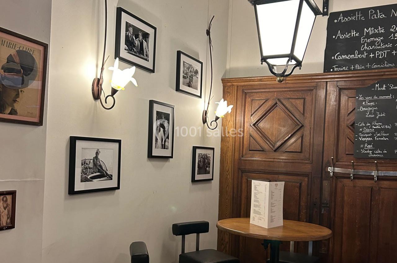 Mur décoré de photos en noir et blanc, éclairé par des appliques et une lanterne, avec une table et des chaises en premier…