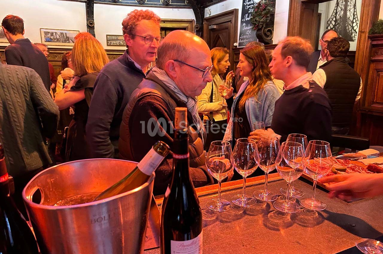 Des personnes discutent autour d'un bar avec des verres à vin et des bouteilles, dans une ambiance conviviale.