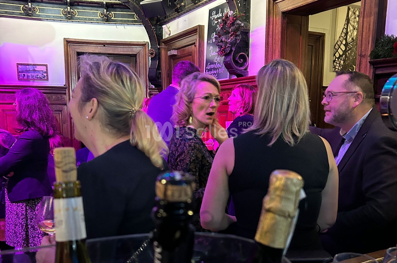 Groupe de personnes discutant dans un bar ou un espace convivial, avec des bouteilles au premier plan.