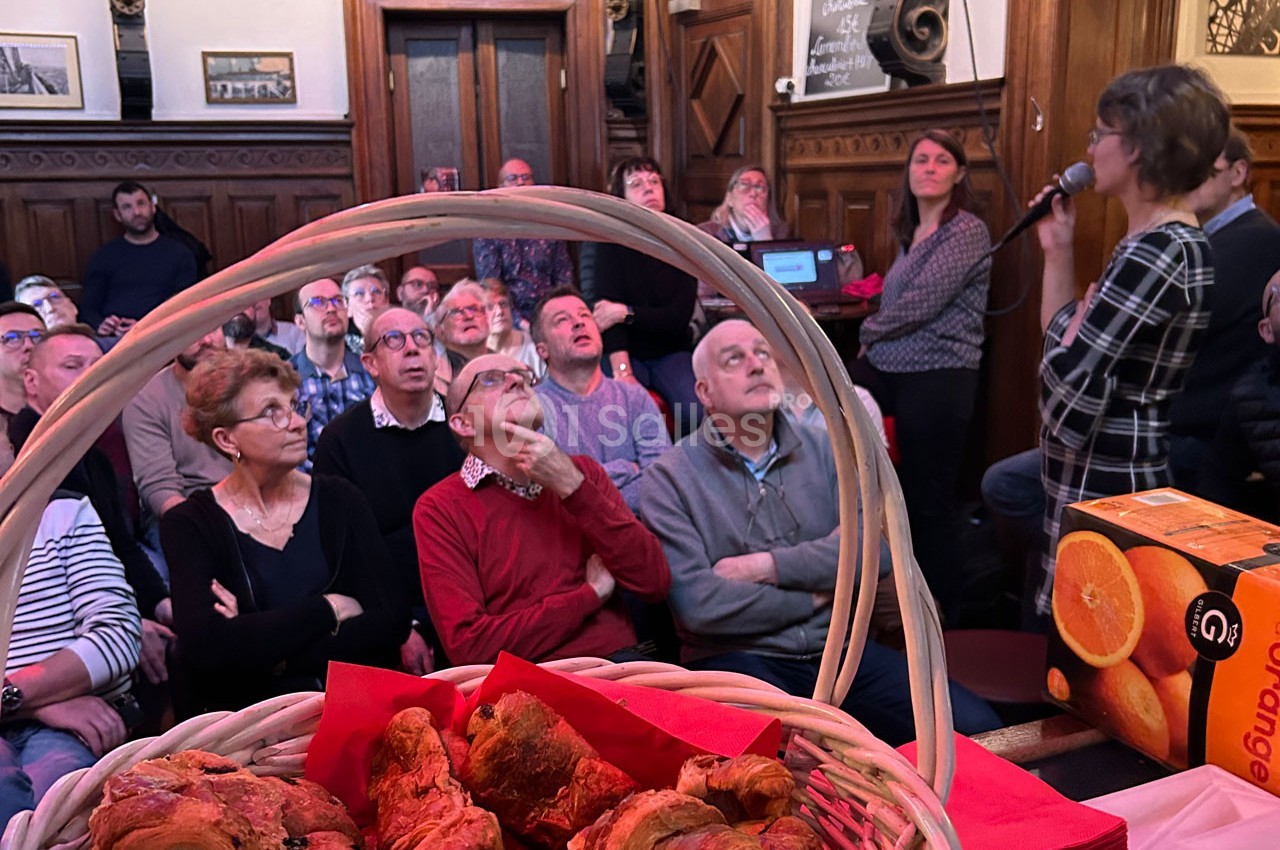 Un groupe de personnes assises écoute une intervenante dans une salle en bois, avec des viennoiseries au premier plan.