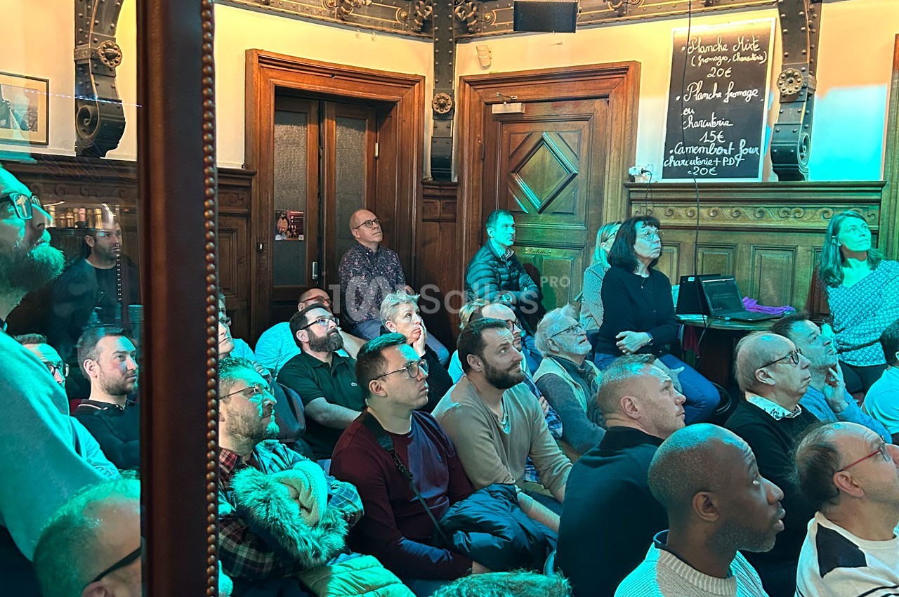 Un groupe de personnes assises et debout dans une salle en bois, regardant attentivement vers l'avant.