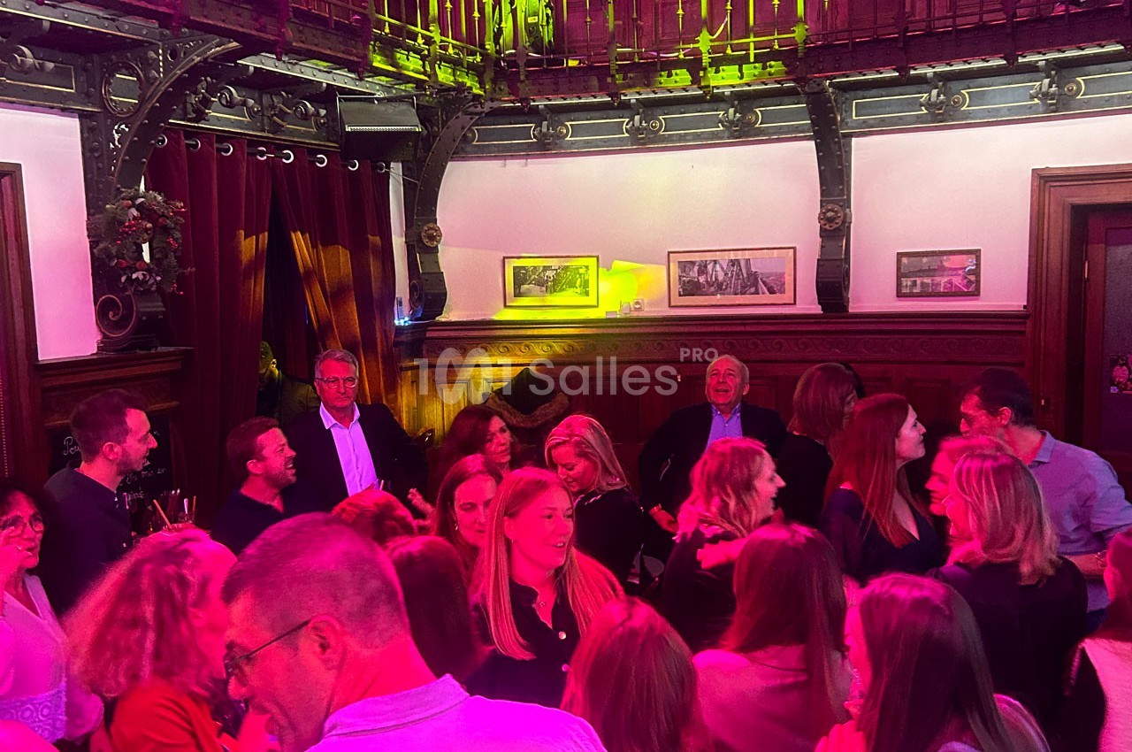 Groupe de personnes discutant et partageant un moment convivial dans une salle à la décoration boisée et éclairage coloré.