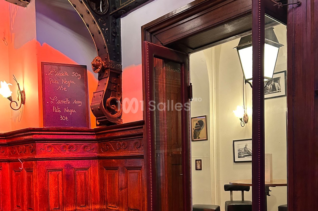 Intérieur d'un restaurant avec boiseries sculptées, tableau de menu à l'ardoise et lampe murale éclairant l'espace.