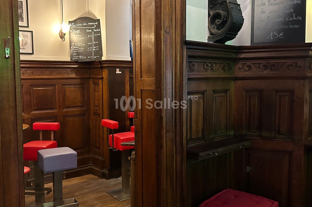 Intérieur d'un café avec boiseries, tabourets rouges et violets, et ardoises murales affichant des menus.