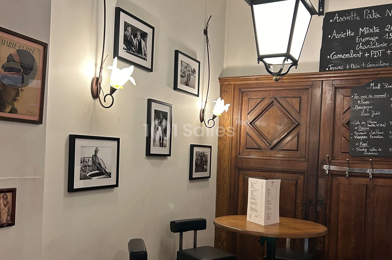 Mur décoré de photos en noir et blanc dans un café, avec une table ronde en bois et un menu posé dessus.