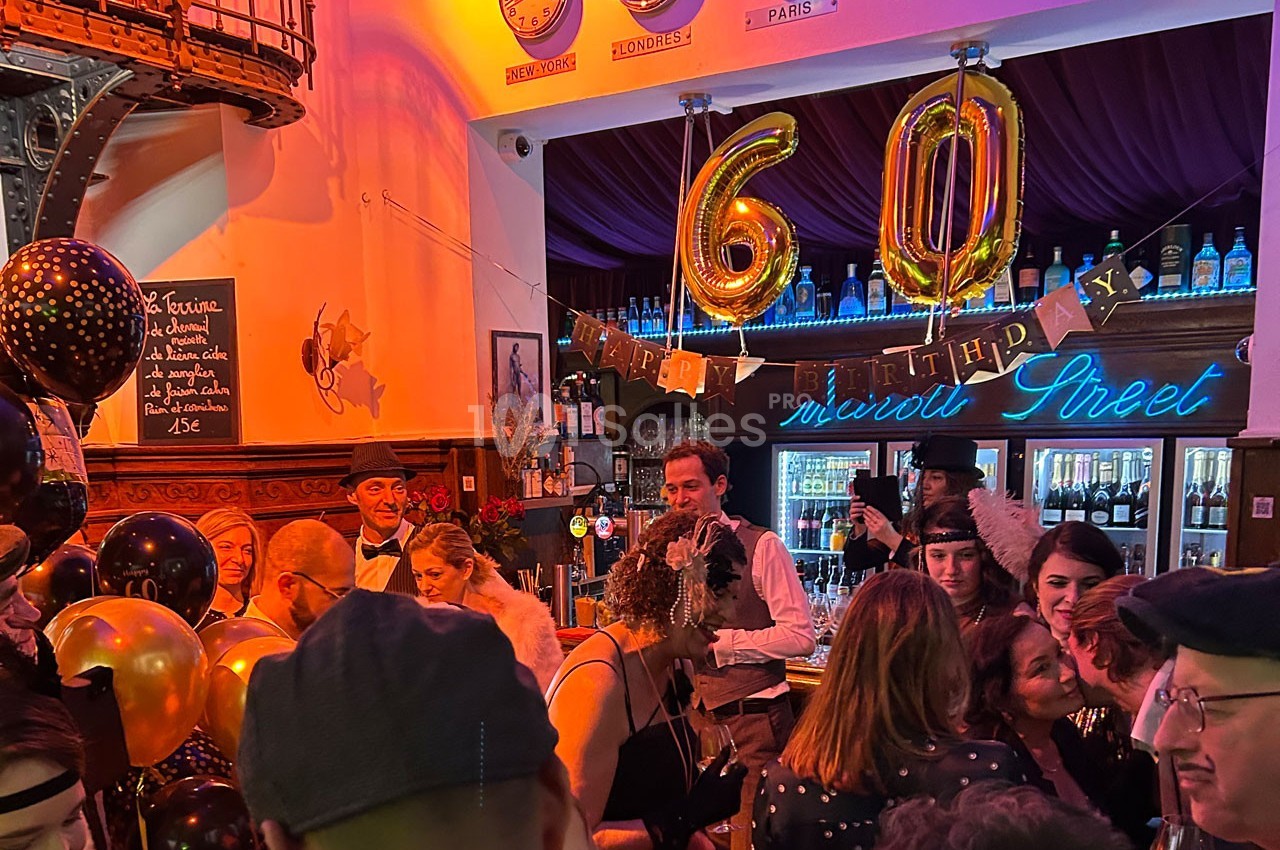 Fête d'anniversaire dans un bar décoré, avec des ballons ’60’ et des invités en tenue élégante.