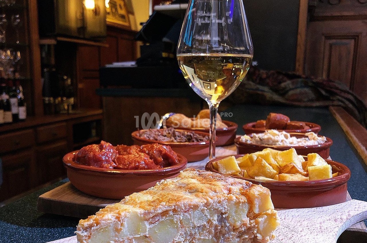 Assortiment de tapas espagnols avec une tortilla, des patatas bravas et un verre de vin blanc sur un comptoir.