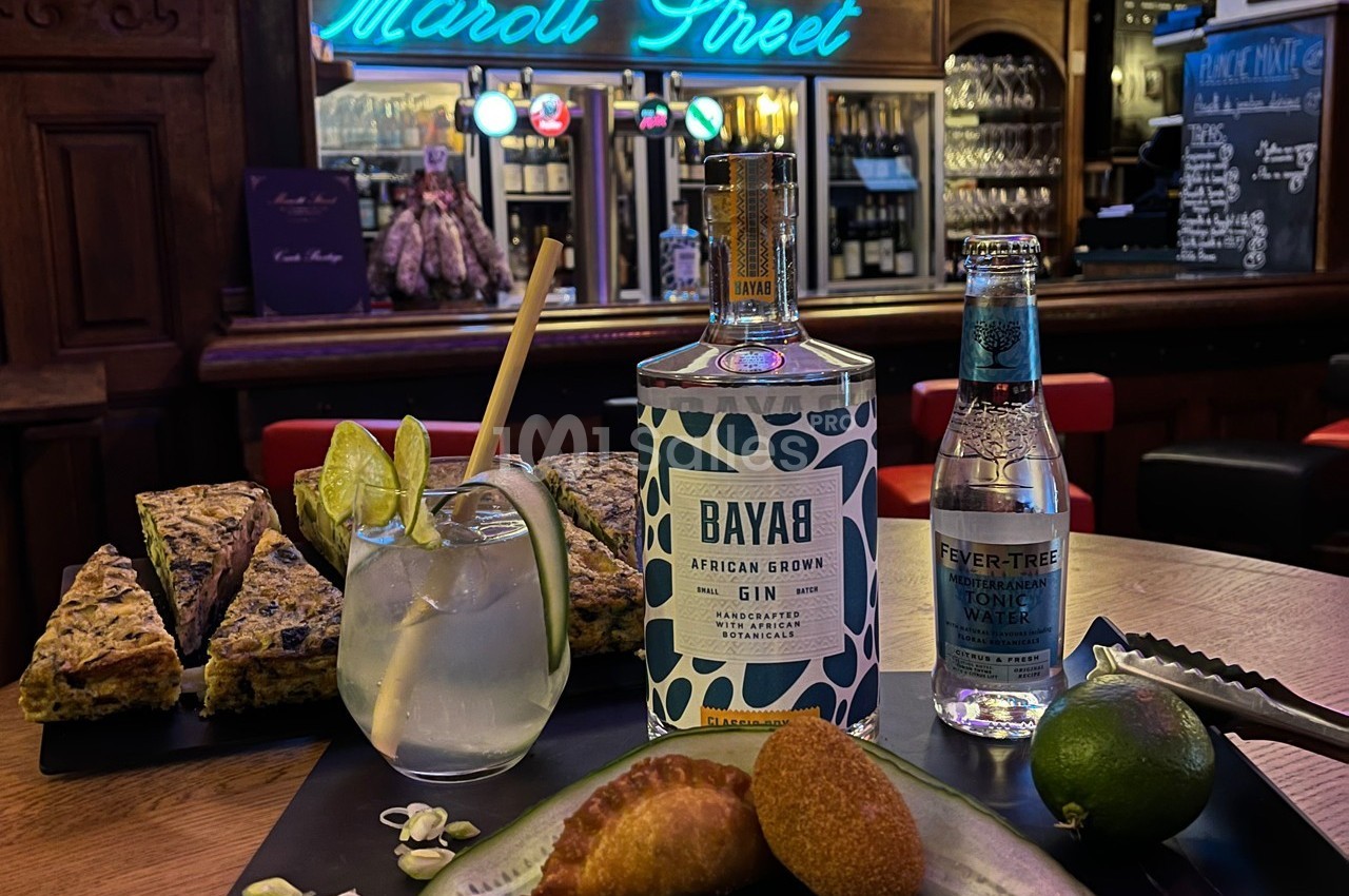 Un bar avec un comptoir garni de gin, tonic, amuse-bouches, citron vert et décor lumineux en arrière-plan.