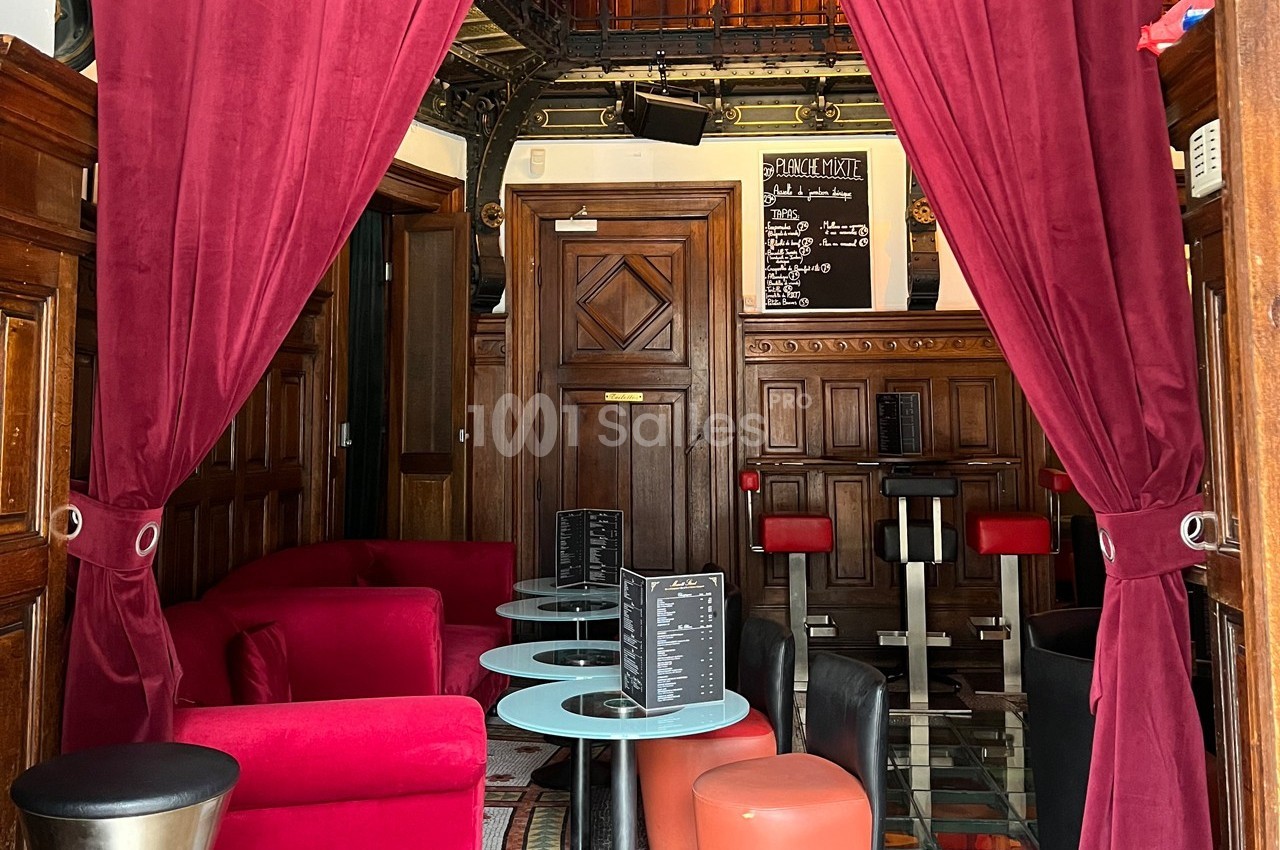 Espace intérieur avec fauteuils rouges, tables basses et rideaux en velours, dans un décor boisé et chaleureux.