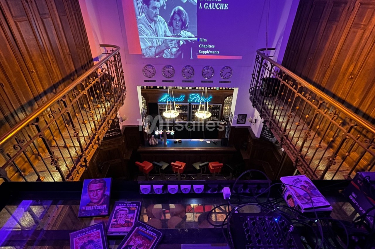 Vue plongeante sur un bar rétro avec une projection de film en arrière-plan et des magazines vintage au premier plan.