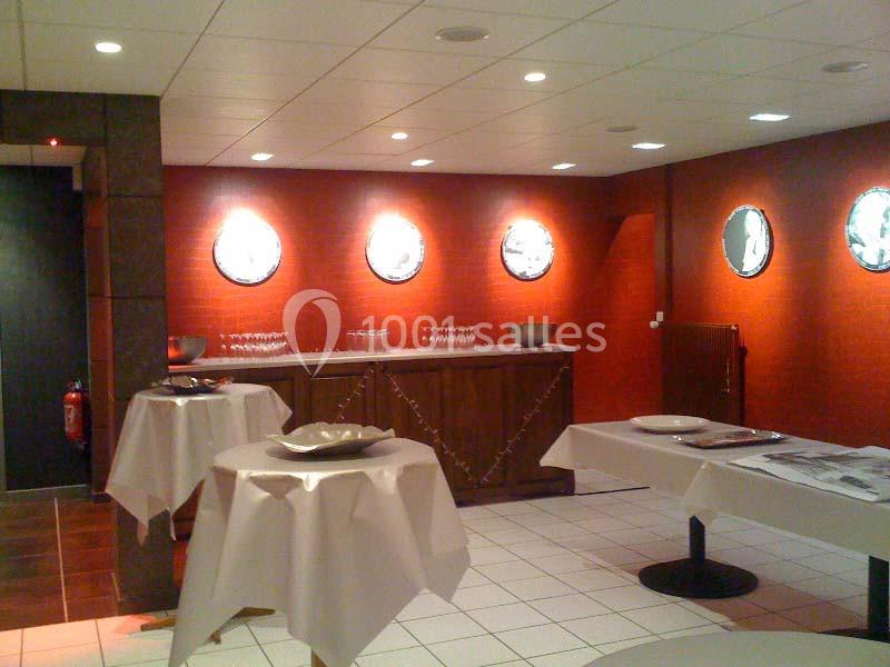 Salle avec murs rouges, tables hautes recouvertes de nappes blanches et un buffet en bois orné de miroirs ronds.