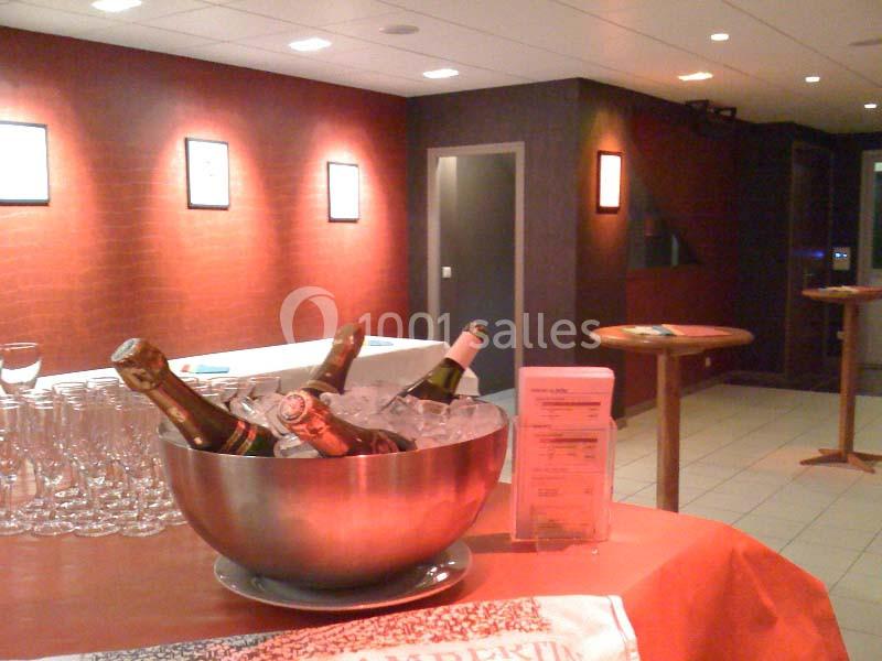 Bol en métal rempli de bouteilles de champagne sur glace, entouré de verres vides dans une salle éclairée.