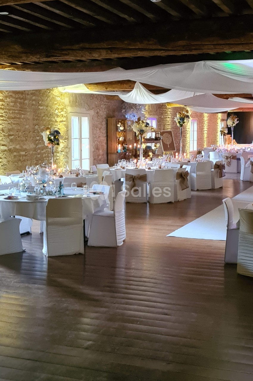 Salle de réception décorée avec des tables rondes, nappes blanches, chaises habillées et éclairage chaleureux.