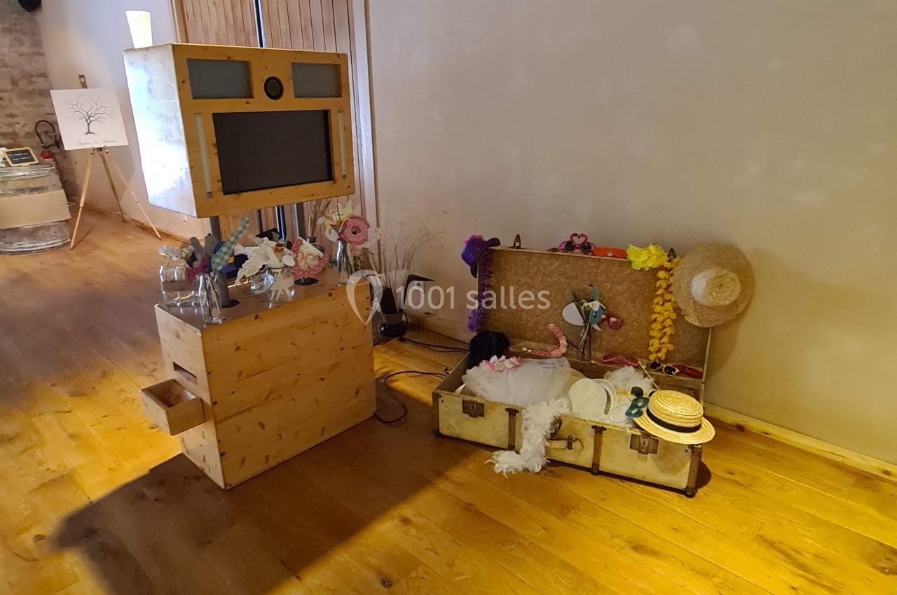 Photobooth en bois avec accessoires colorés disposés sur des valises anciennes dans une salle au sol en parquet.