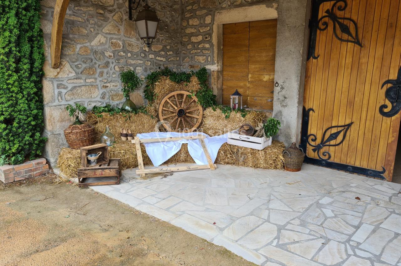Décoration rustique avec bottes de paille, roue en bois, lanternes et objets anciens devant une porte en bois sculpté.