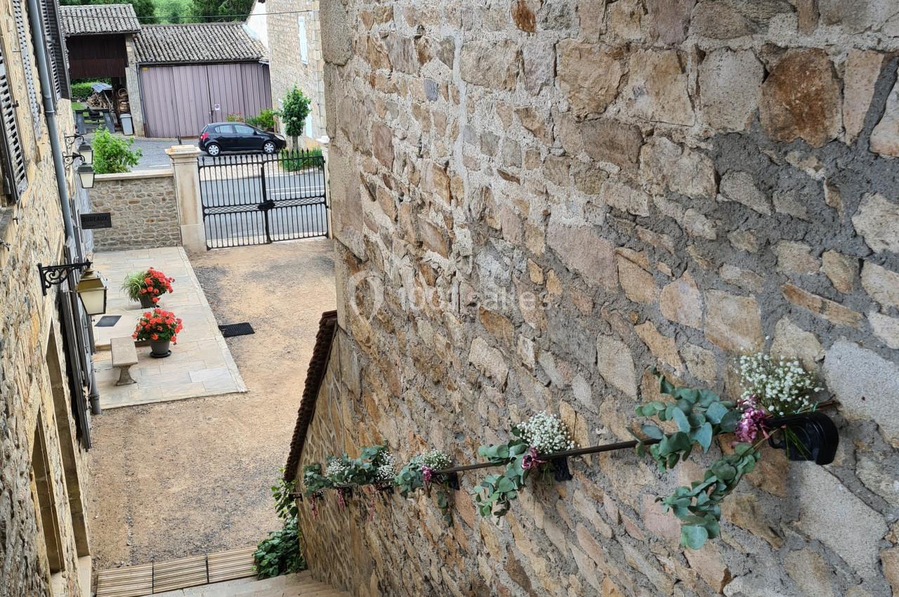 Escalier en pierre bordé de fleurs, menant à une rue pavée avec vue sur des bâtiments et une campagne vallonnée.