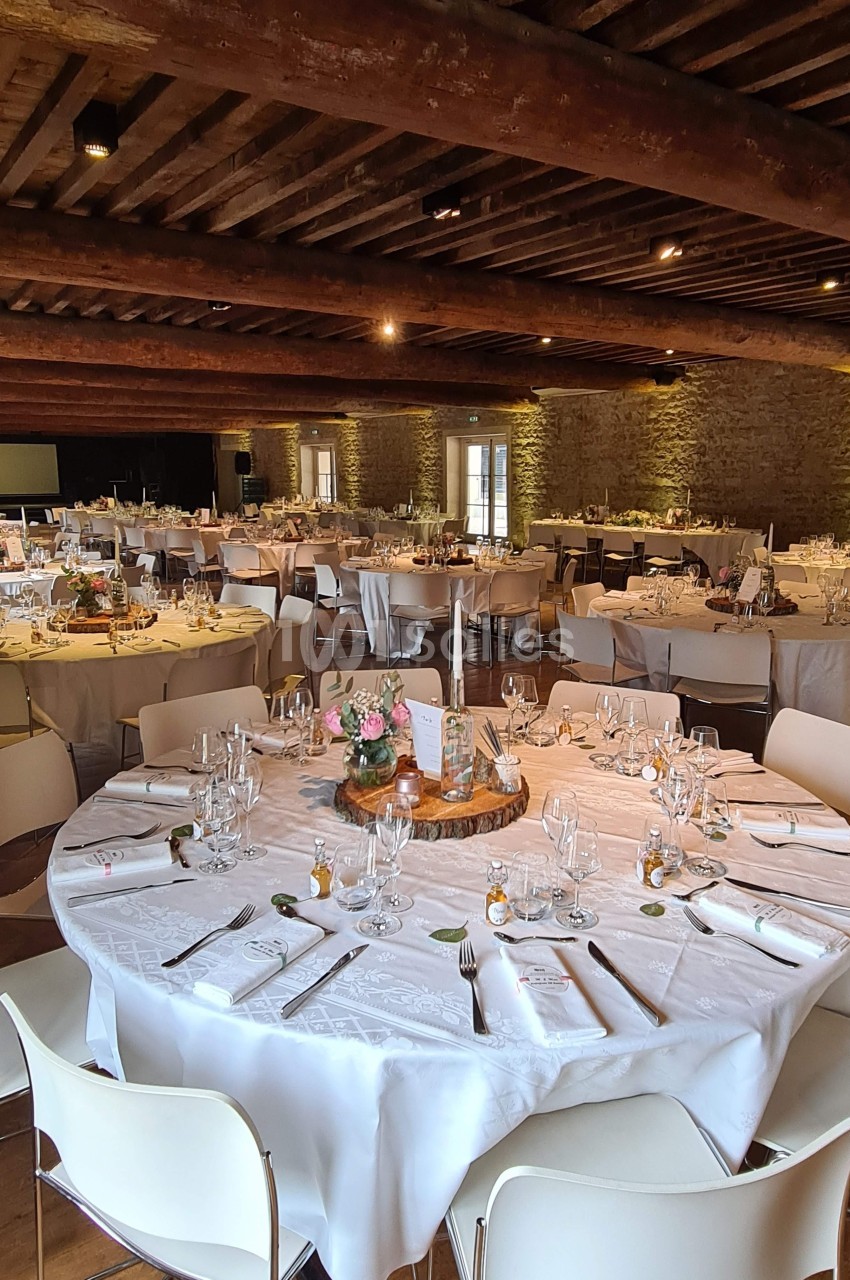 Salle de réception avec tables rondes élégamment dressées, nappes blanches et décoration florale.