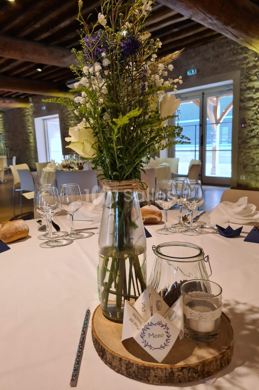 Centre de table avec bouquet champêtre dans un vase en verre, posé sur une rondelle de bois avec menu et bougie.