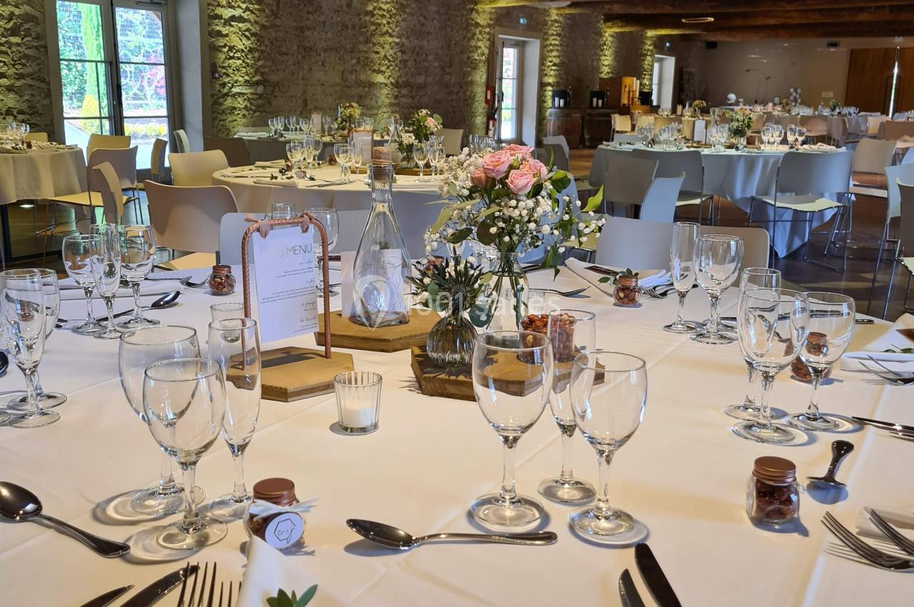 Salle de réception décorée pour un mariage, avec tables rondes dressées, fleurs et vaisselle élégante.
