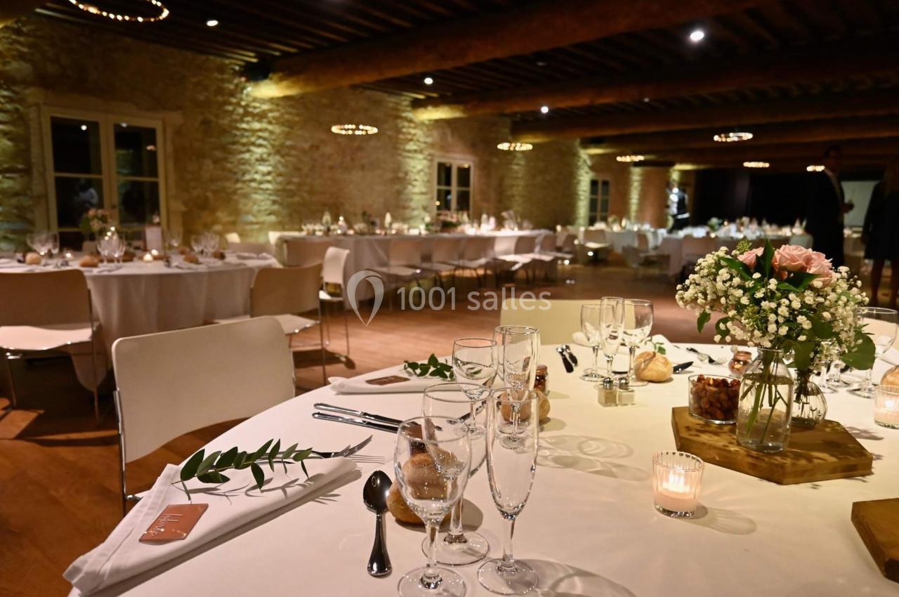 Salle de réception élégante avec tables décorées de fleurs, bougies et vaisselle, ambiance chaleureuse en soirée.