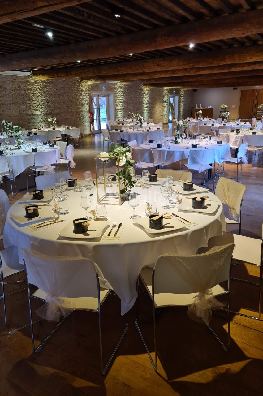 Salle de réception décorée avec des tables rondes dressées, nappes blanches et centres de table fleuris.