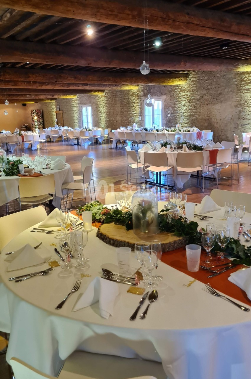Salle de réception décorée avec des tables rondes dressées, nappes blanches, et centre de table floral.