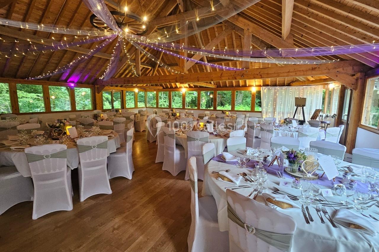 Salle de réception décorée avec des tables rondes dressées, des chaises blanches et des guirlandes lumineuses suspendues.