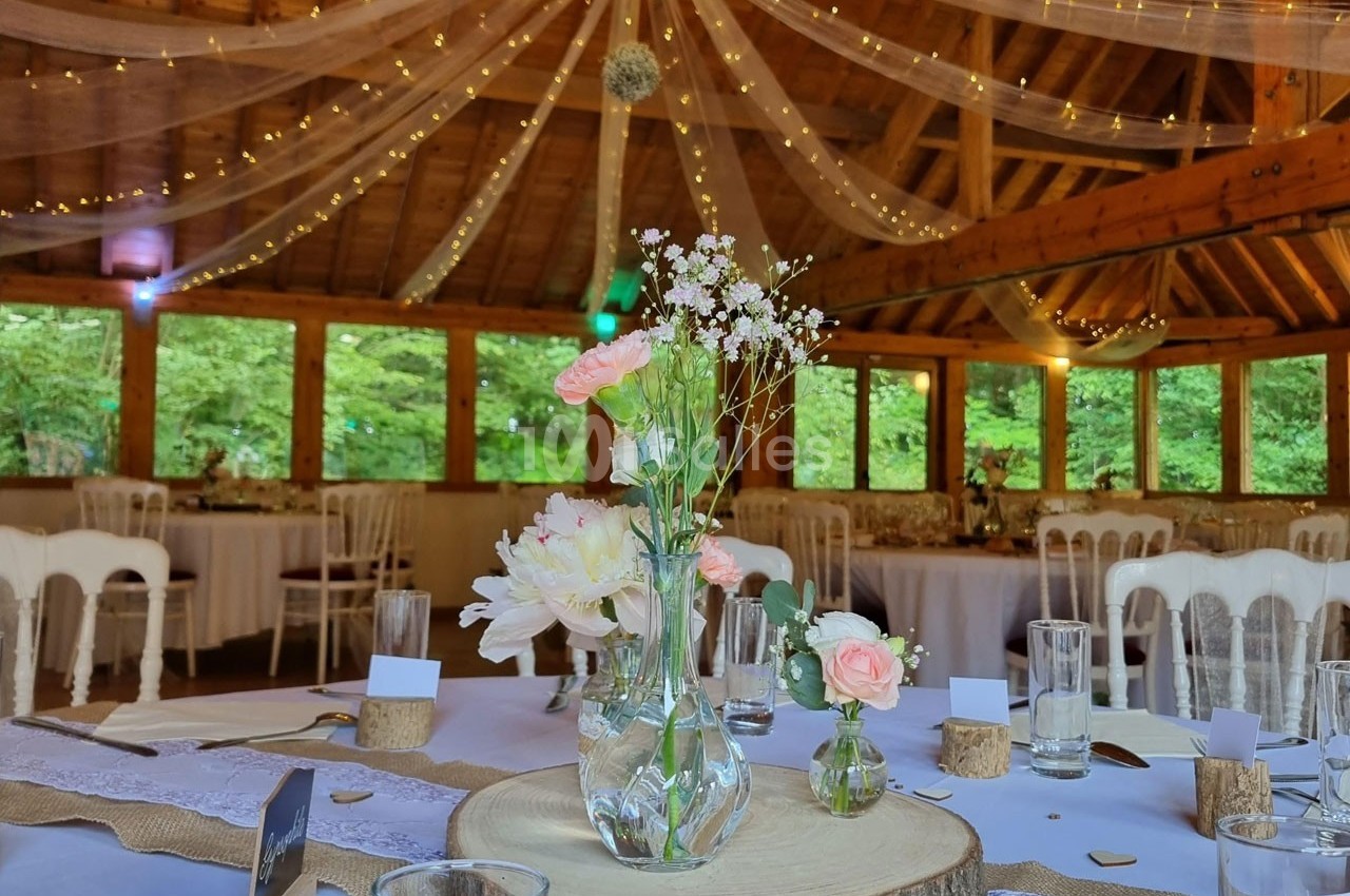 Salle de réception en bois décorée avec des guirlandes lumineuses, des fleurs et des tables dressées pour un événement.