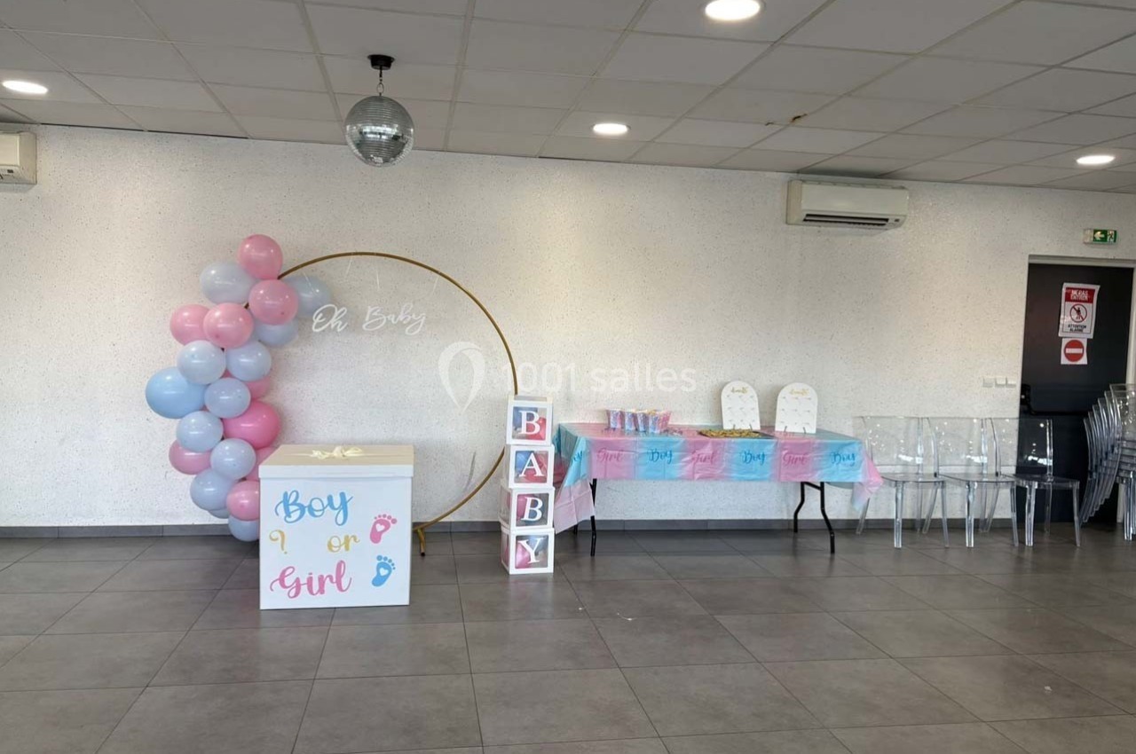 Salle décorée pour une fête de révélation de genre, avec ballons roses et bleus, table dressée et cubes ’BABY’.