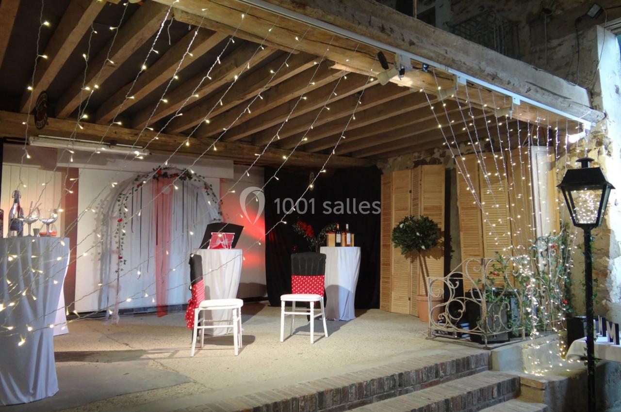 Location salle La Villeneuve-en-Chevrie (Yvelines) - La Grange des Mollières #8 Décoration lumineuse avec guirlandes suspendues dans un espace couvert, comprenant des chaises et des tables décorées.