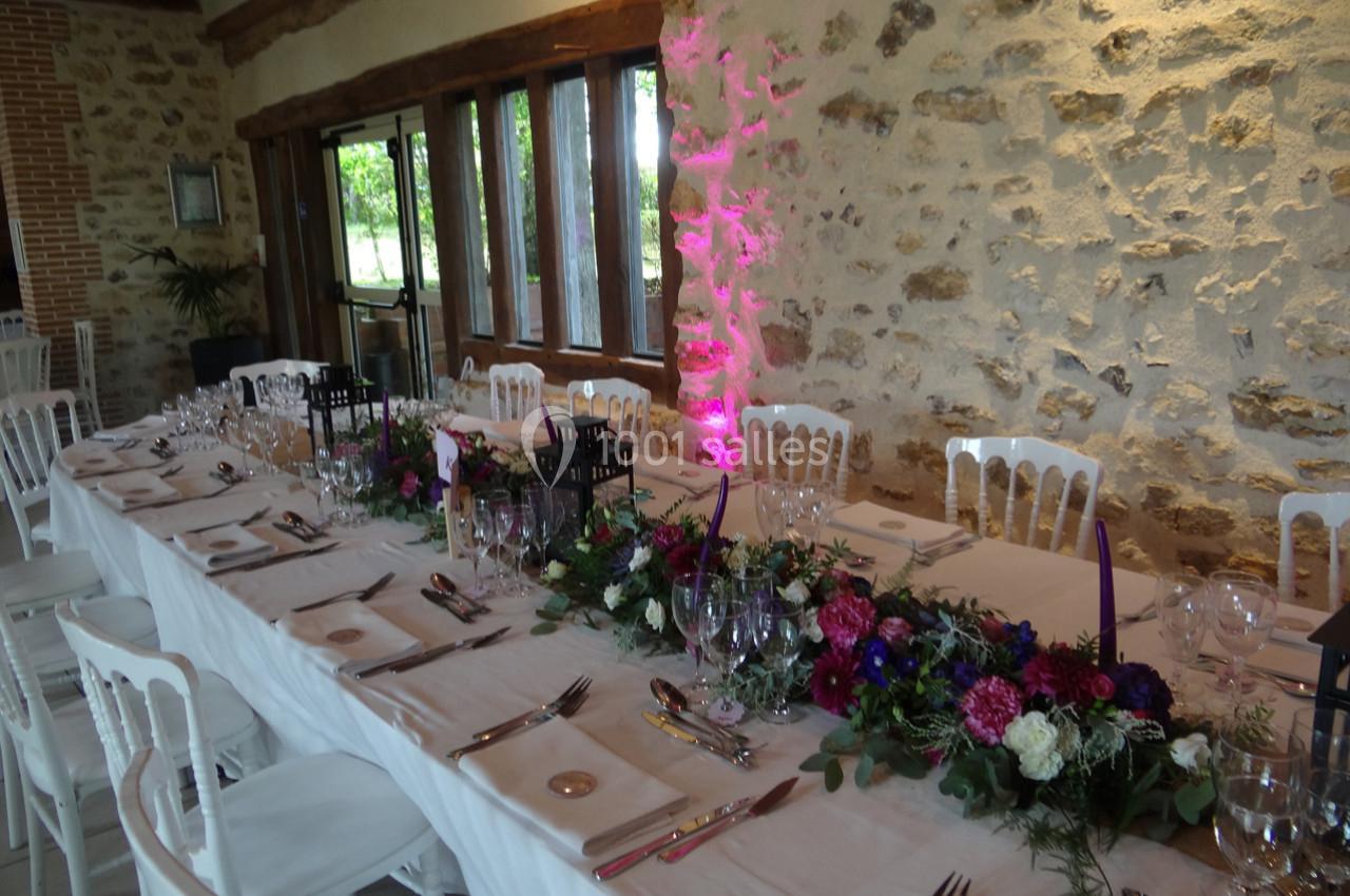 Location salle La Villeneuve-en-Chevrie (Yvelines) - La Grange des Mollières #13 Table de réception décorée avec nappes blanches, compositions florales colorées et lanternes, dans une salle en pierre…