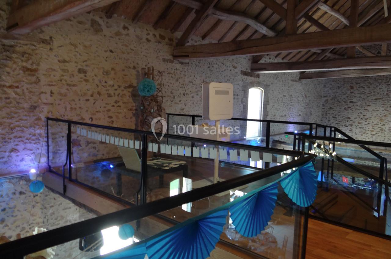 Location salle La Villeneuve-en-Chevrie (Yvelines) - La Grange des Mollières #12 Mezzanine avec sol en verre, rambardes en métal et décoration bleue dans un intérieur en pierre apparente.