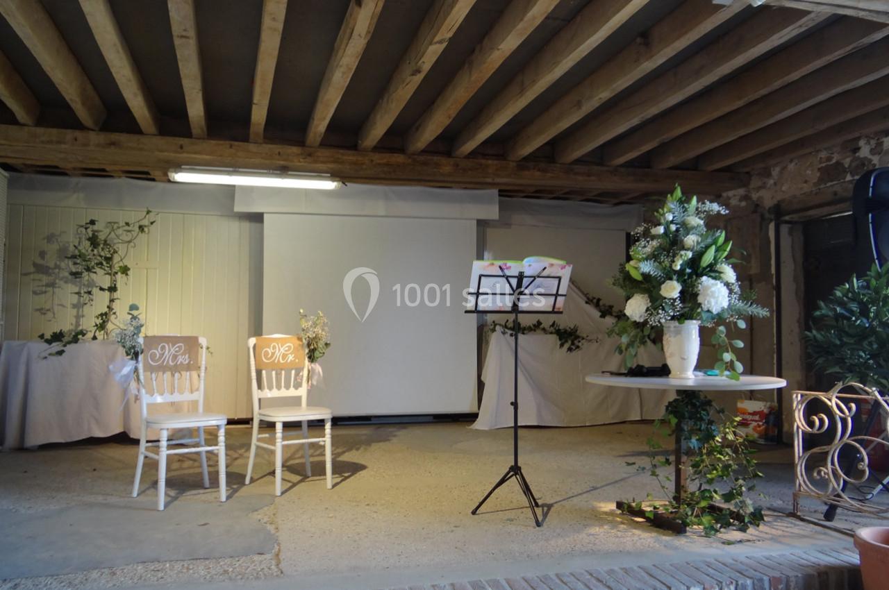 Location salle La Villeneuve-en-Chevrie (Yvelines) - La Grange des Mollières #14 Deux chaises décorées, un pupitre et des arrangements floraux dans une salle avec poutres apparentes.