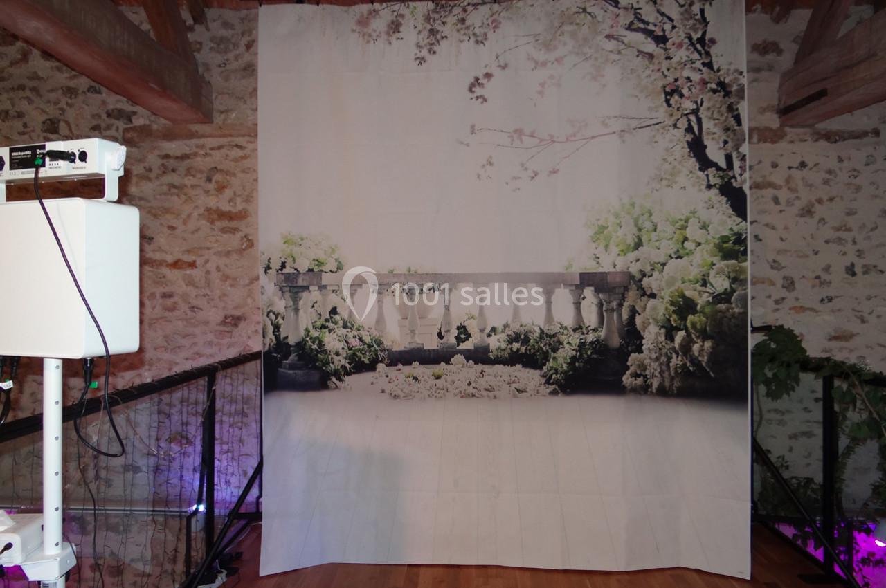 Location salle La Villeneuve-en-Chevrie (Yvelines) - La Grange des Mollières #26 Rideau imprimé représentant une balustrade entourée de végétation, installé dans une pièce avec poutres apparentes.