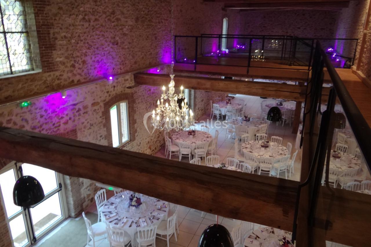 Location salle La Villeneuve-en-Chevrie (Yvelines) - La Grange des Mollières #30 Salle de réception en pierre avec tables rondes dressées, lustre central et éclairage violet tamisé.
