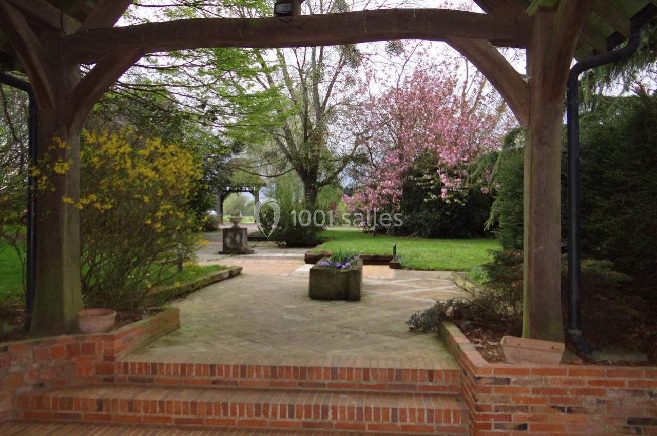 Location salle La Villeneuve-en-Chevrie (Yvelines) - La Grange des Mollières #33 Vue d'un jardin fleuri avec un cerisier en fleurs, encadré par une structure en bois et des marches en briques.