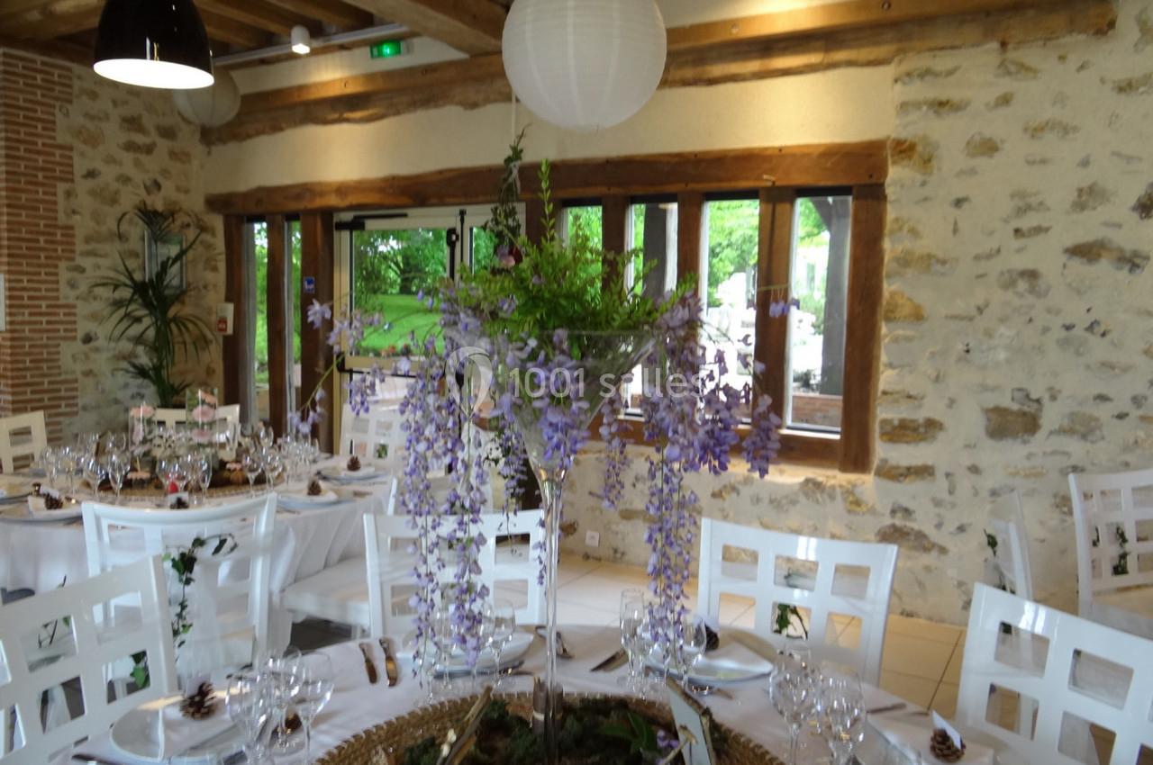 Location salle La Villeneuve-en-Chevrie (Yvelines) - La Grange des Mollières #31 Salle de réception lumineuse avec tables dressées et centre de table floral composé de glycines violettes.