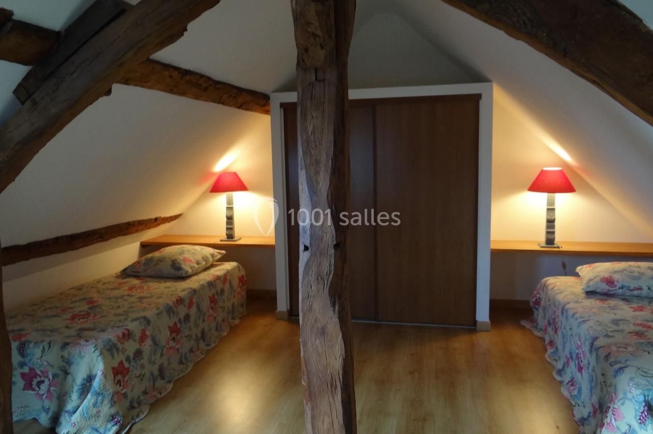 Location salle La Villeneuve-en-Chevrie (Yvelines) - La Grange des Mollières #52 Deux lits simples sous des poutres apparentes dans une chambre mansardée avec lampes de chevet et parquet au sol.