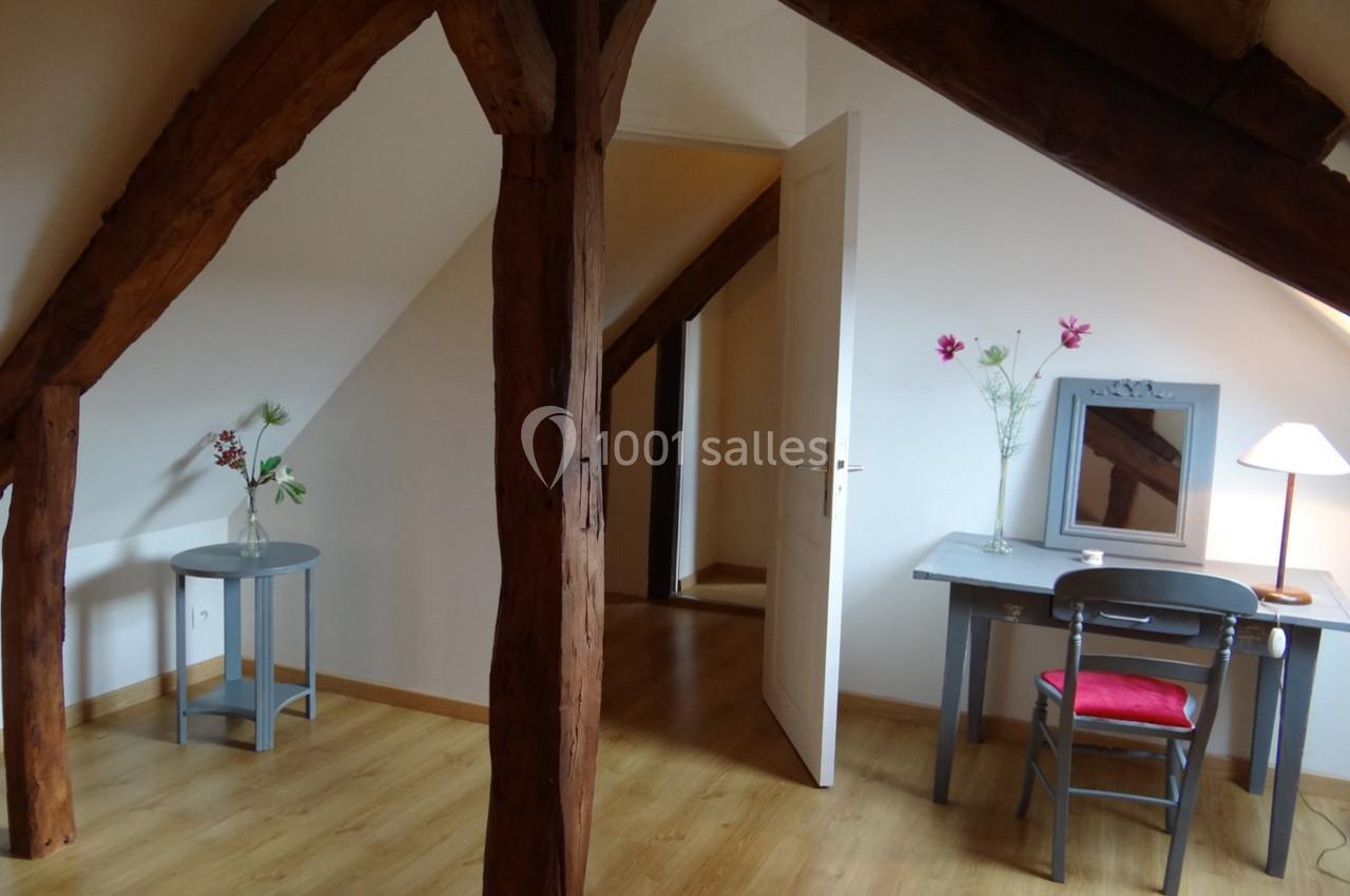Location salle La Villeneuve-en-Chevrie (Yvelines) - La Grange des Mollières #53 Pièce mansardée avec poutres apparentes, un bureau, une chaise, une lampe et des fleurs sur des meubles en bois.
