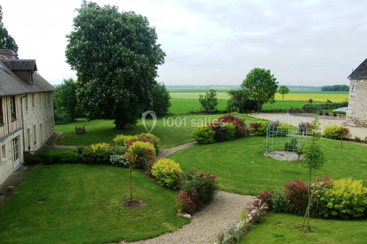 Location salle La Villeneuve-en-Chevrie (Yvelines) - La Grange des Mollières #34 Jardin paysager avec pelouse, massifs fleuris, allées gravillonnées, tonnelle métallique et bâtiments en pierre.