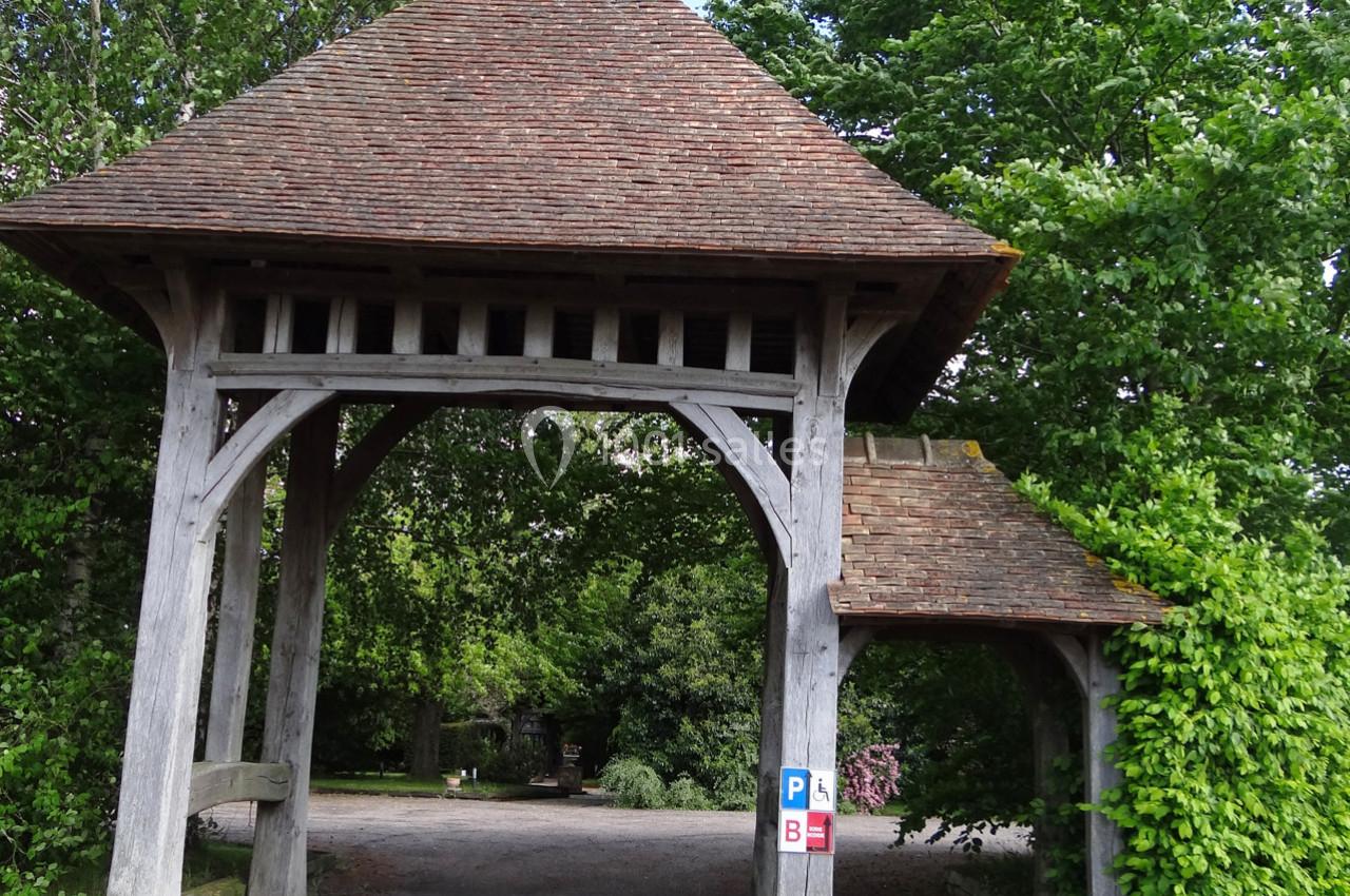 Location salle La Villeneuve-en-Chevrie (Yvelines) - La Grange des Mollières #35 Portail en bois avec toit en tuiles, entouré de végétation, donnant accès à un chemin gravillonné.