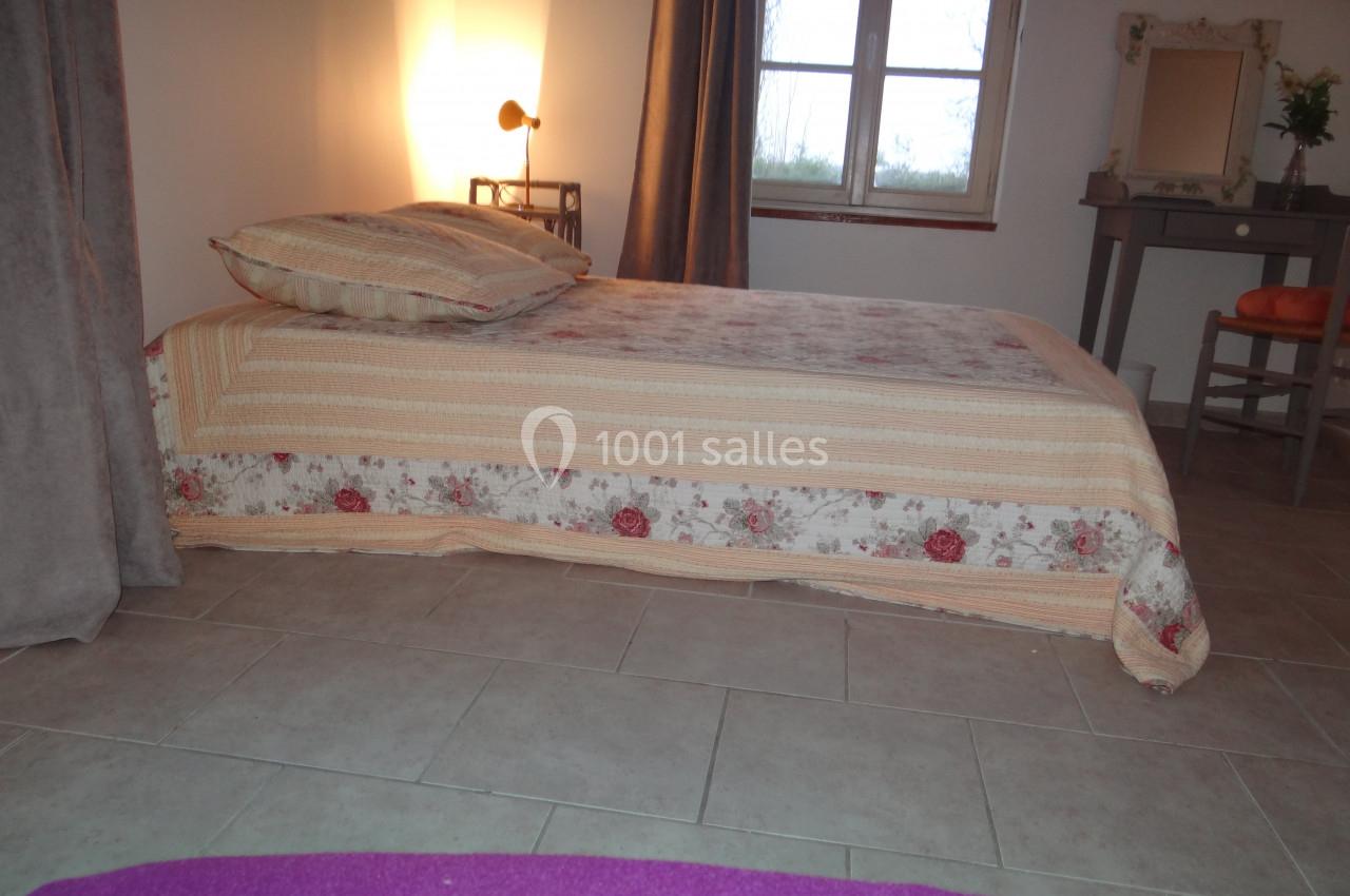 Location salle La Villeneuve-en-Chevrie (Yvelines) - La Grange des Mollières #57 Lit simple avec couvre-lit fleuri dans une chambre lumineuse, éclairée par une lampe de chevet près d'une fenêtre.