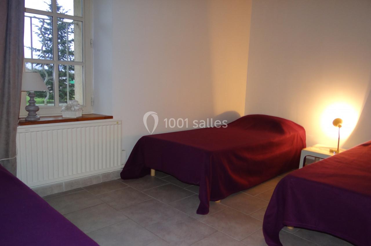 Location salle La Villeneuve-en-Chevrie (Yvelines) - La Grange des Mollières #56 Deux lits simples avec couvre-lits violets dans une chambre lumineuse avec fenêtre, lampe de chevet et sol carrelé.